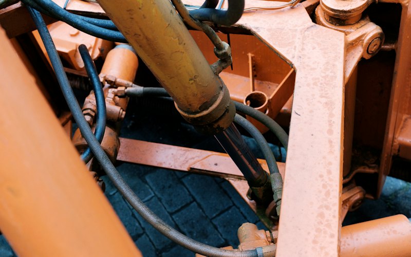 Vérin hydraulique et flexibles noirs sur le châssis orange d'un engin