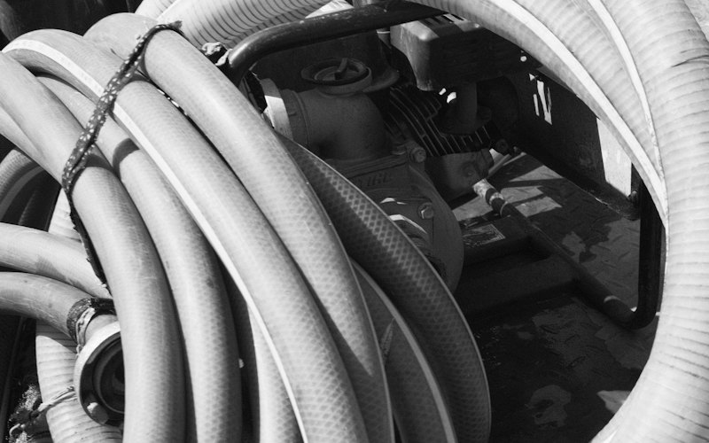 Tuyaux souples enroulés à côté d'une motopompe, photo en noir et blanc